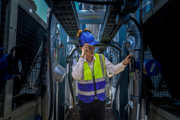 An industrial worker in high-visibility gear and a blue helmet meticulously examines the intricate...