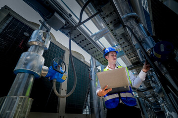 An industrial worker in high-visibility gear and a blue helmet meticulously examines the intricate network of machinery. The engineer is dedicated to maintaining operational efficiency and safety.