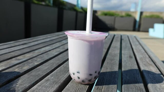 sticking a straw into a bubble tea (milk based drink with tapioca balls on picnic table outside) poking plastic cup large straw