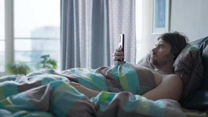 Man holding smartphone lying in bed in the morning, shoked, surprised by an important message. Important morning breaking news. Smartphone news addiction