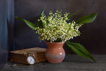 bouquet of lilies of the valley on a dark background. An old, battered book and a pocket watch with a chain.
