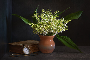 bouquet of lilies of the valley on a dark background. An old, battered book and a pocket watch with a chain.