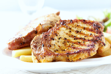 Grilled Steaks with french fries and fresh salad. Bright wooden background.	