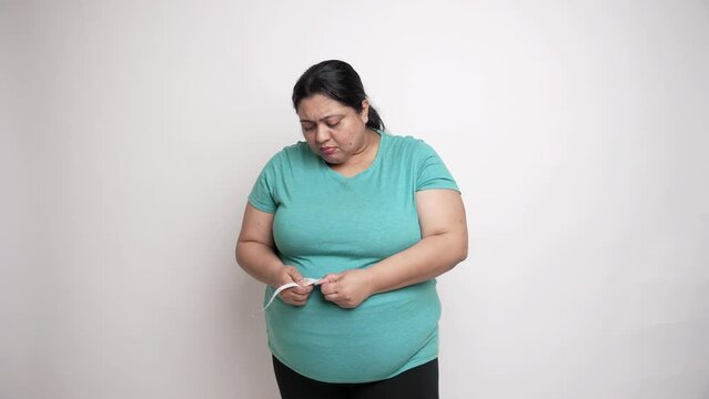 Oversize indian woman feeling sad after measuring her waist isolated over white background. Asian Plus size female Check belly fat, Obesity and weight loss concept,4k