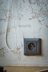 White Bead Chain Hanging On Distressed White Wall Beside Grey Electrical Outlet