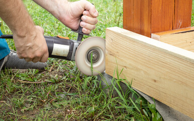 A close-up shot of a worker using a grinder to shape a wooden beam outside on a sunny day.
