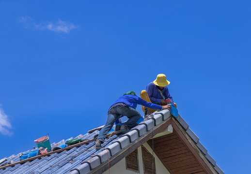 Workers Repairman repairing leaking ridges tile roofing and replace cracked broken tile roofing on  blue  sky  background.