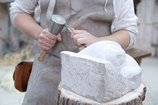 Close up of young sculptor hands working on his marble sculpture in his workshop with hammer and chisel