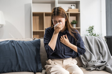 A young female Asian is sitting on a sofa, wrapped in a shawl. She is experiencing cold symptoms...