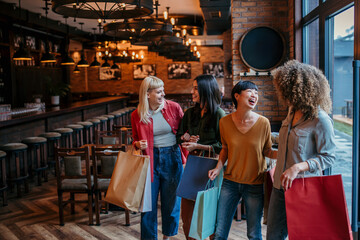 Fototapeta premium A group of diverse female friends walking into a restaurant, chatting happily with shopping bags in hand