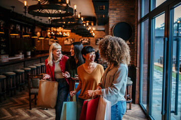 Fototapeta premium A group of diverse female friends walking into a restaurant, chatting happily with shopping bags in hand