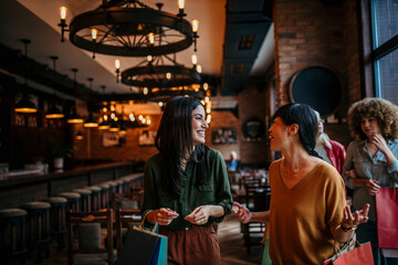 Female friends chatting and smiling, walking into a restaurant carrying shopping bags