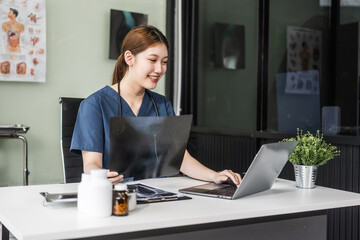 A young Asian nurse providing online consultations, seated at her desk with a laptop. She offers...
