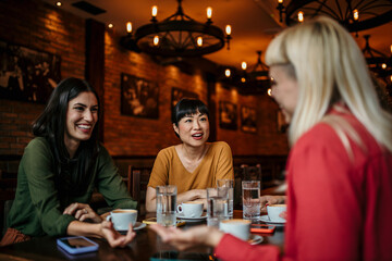 Three Young Female Friends Meeting Sit At Table In Coffee Shop And Talk