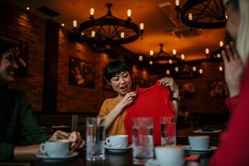 Smiling Asian woman showing her friends what clothes she bought in shopping, they are in the restaurant