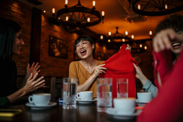 A smiling woman in a restaurant showing to her friends new clothes that she bought, while enjoying a coffee