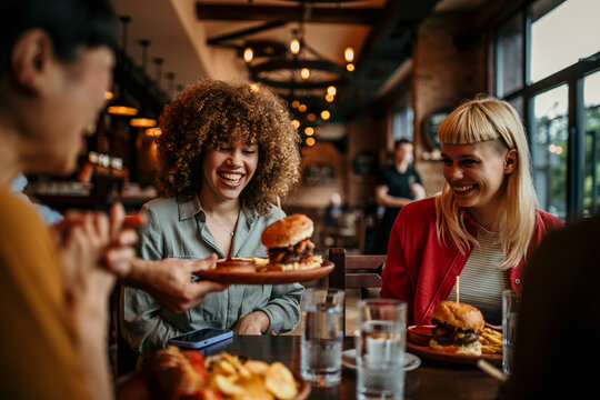 Waiter serving burger to a group of friends having lunch at a restaurant - food service concepts