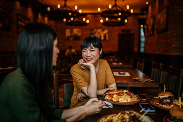 Two female friends sitting and casually chatting during a lunch in the restaurant. Copy space