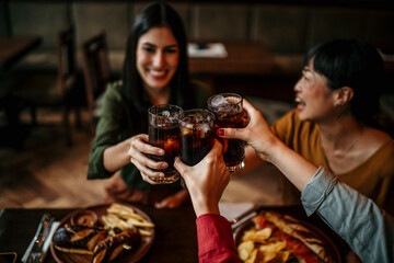 Multi-ethnic group of friends sitting in restaurant and cheering with soft drinks