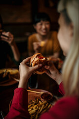 Unrecognizable woman holding a burgers in hands and about to eat it while having a lunch with her...