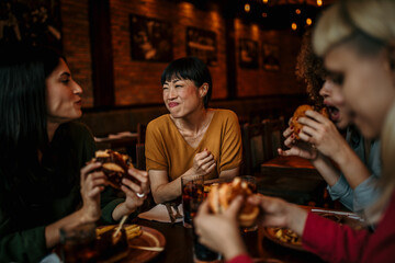 Group Of Young Friends Meeting For Drinks And Food In Restaurant. Focus On A Smiling Asian Woman Talking And Eating
