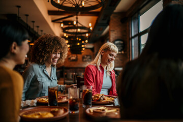 Cheerful diverse female friends packing their stuff and walking out from a table after a lunch in the restaurant