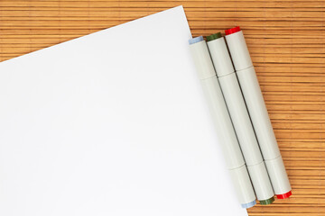 three markers for sketching laying at sheet of white paper on bamboo mat