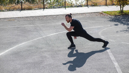 Fototapeta premium Bearded man with long hair doing lunges on the sports field. 