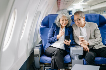 Smiling senior couple of Asian tourists take photos of each other while sitting on a plane. with...