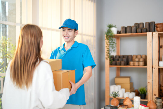 Smiling delivery person in blue uniform hands packages box to a customer indoors showcasing reliable and friendly delivery service