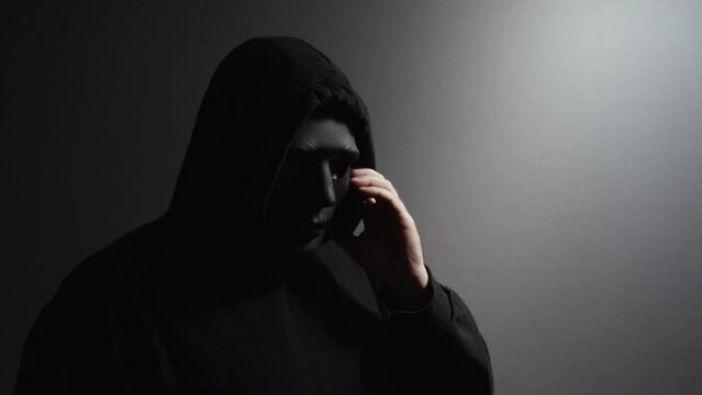 Phone Scammers, man in a mask with a phone, cyber theft and fraud, mobile phone used for hacking, secret attacks on privacy.