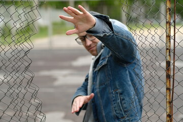 A Man with glasses in a Denim Jacket Dances Near a Chain Link Fence