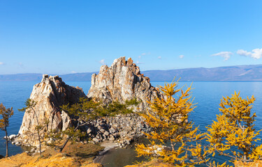 Obraz premium Lake Baikal in autumn. The famous Shamanka rock framed by yellowed larches on a sunny October morning. Traveling around the autumn island of Olkhon. Picturesque landscape. Natural background