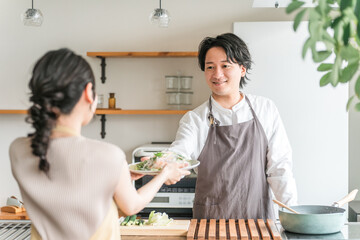 キッチンで料理をする・渡す若いアジア人夫・（料理男子・自炊・共働き・ディンクス・趣味）
