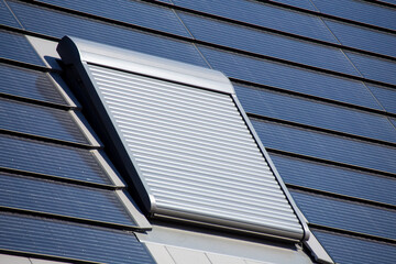 Dachfenster mit Rollladen an einem Einfamilienhaus mit Photovoltaikziegel. Photovoltaikziegel sind...