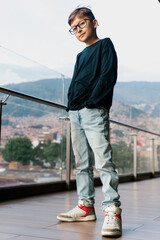 Blond-haired Latino boy with glasses, happy on a high floor of a building. Portrait, childhood, model. Landscape and children.