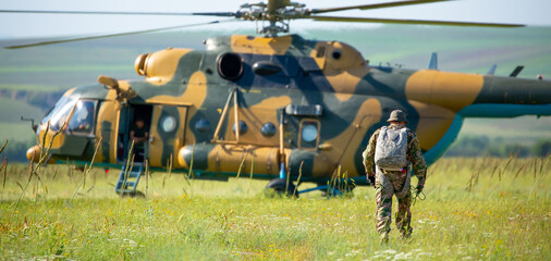 A soldier in camouflage goes to a military helicopter. Military helicopter with soldiers. Armed...