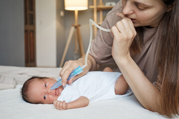 Loving mother using baby nasal aspirator mucus nose suction loving mommy cleaning her infant's nose with a suction pump treating her child's congestion