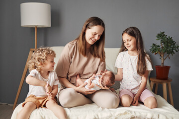 Smiling brown haired Caucasian woman holding newborn son in hands showing infant kid to older daughters family enjoying first meeting with cute tine baby boy