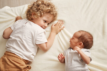 Happy toddler with her brother. Caucasian siblings at home. Cute brother and sister moments. Curious wavy haired older sister with newborn baby
