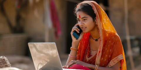 Indian woman in traditional attire using a laptop and talking on phone outdoors