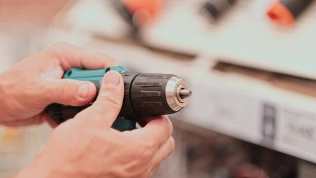 man in a hardware store chooses a new screwdriver or drill next to a showcase of power tools for repairs in the house. hands closeup with tool. 4K