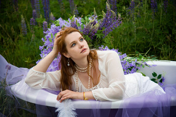 portrait of beautiful romantic readhead bride in vintage white wedding dress relaxing in bath in...