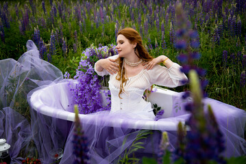 portrait of beautiful romantic readhead bride in vintage white wedding dress relaxing in bath in...