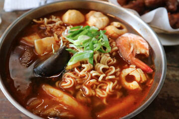 a bowl of noodles or ramyeon with a mixture of green mussels, shrimp, fish balls, meatballs with red tom yum-like. sauce. Korean noodles. Ramen street food.