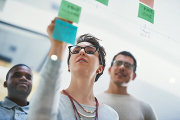 Female speaker, interns and sticky notes on glass for timeline, writing and brainstorming in...