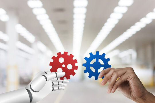 Human and Robotic holding gear from at factory and warehouse background, collaboration innovation concept.