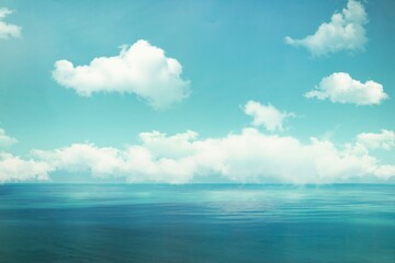An image of a calm ocean with turquoise water and gentle waves. Above, a bright blue sky is dotted with fluffy white clouds. The scene is calm and conveys a feeling of peace and space.