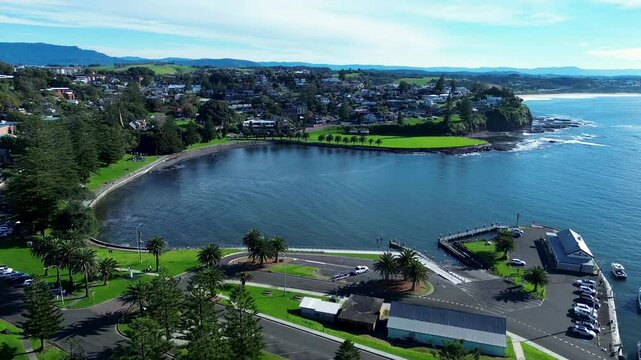 Landscape drone aerial view of Kiama harbour carpark blowhole wharf pier bay headland with residential housing suburbs South Coast Australia travel tourism