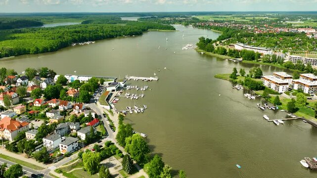 Aerial view of a tranquil lakeside Iława town with boats docked at marinas and lush green surroundings. The scene captures the serene atmosphere and natural beauty of the area